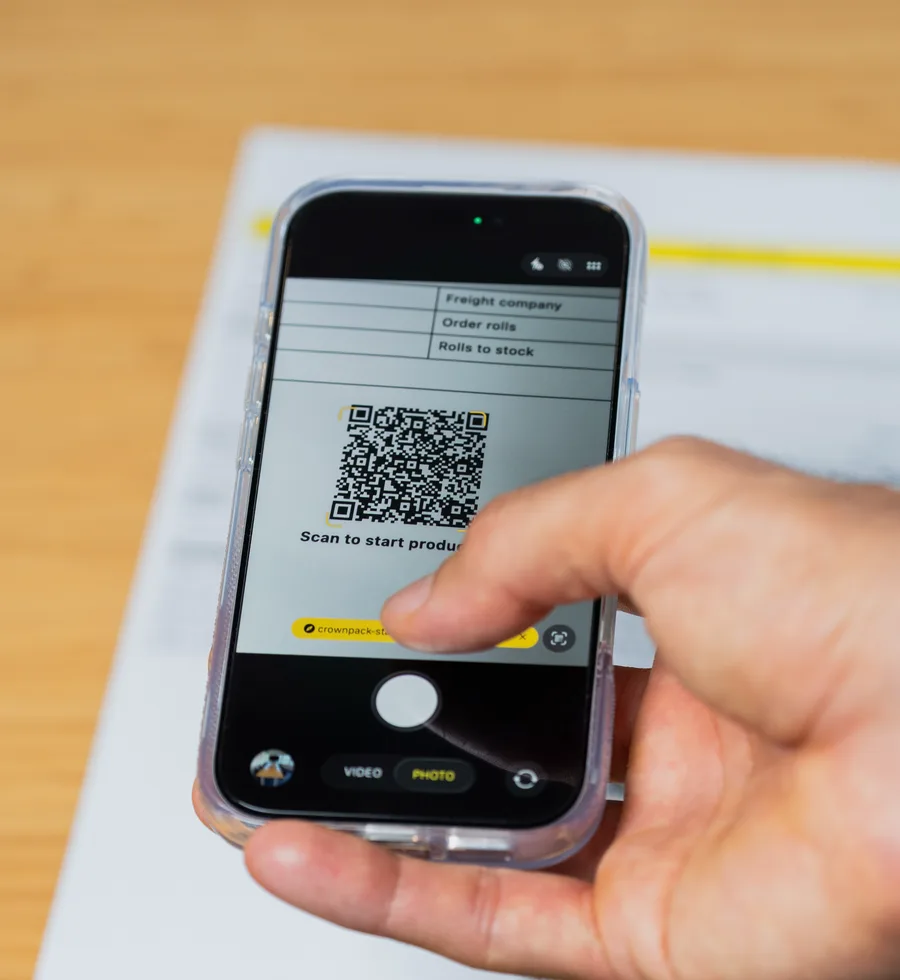 A phone scanning the QR code on a paper job sheet to start production in the Crownpack system