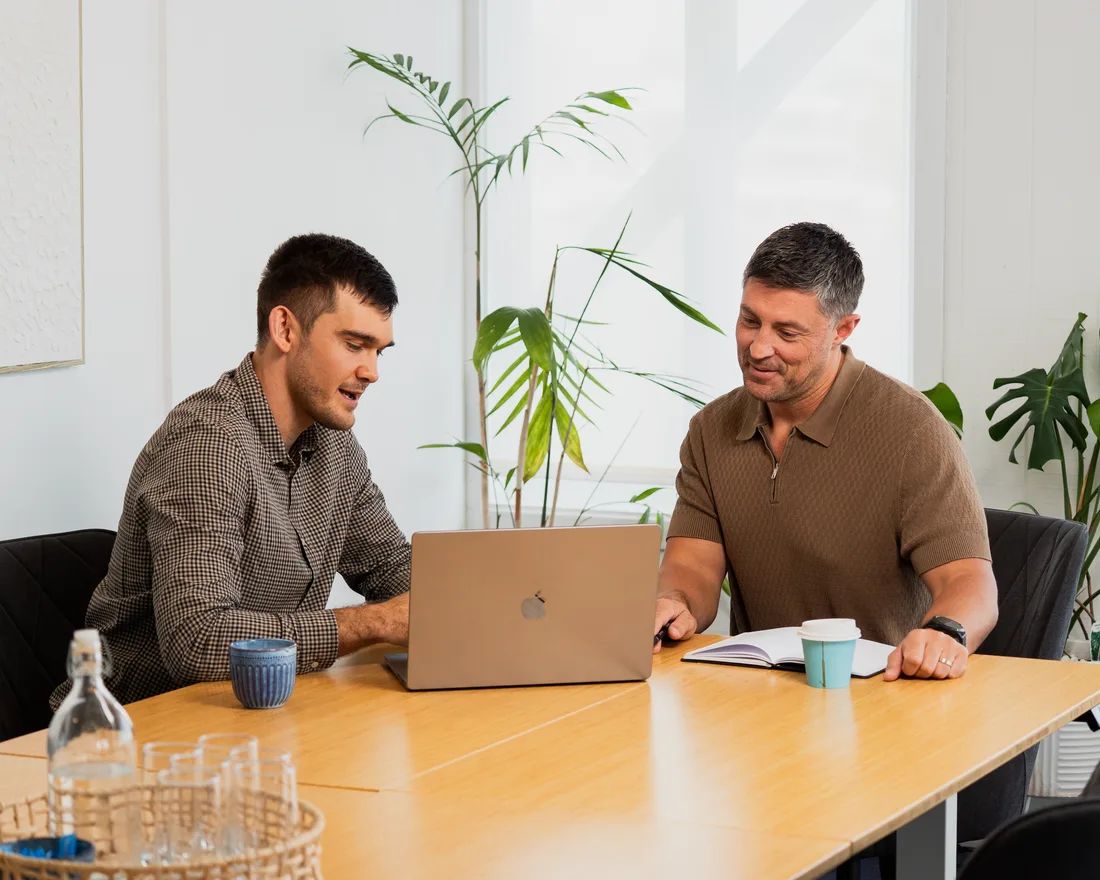 Two people reviewing production software on a laptop in a light-filled boardroom